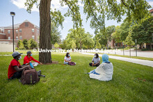 A group of students wearing masks and practice social distancing hangout under a tree on City Campus