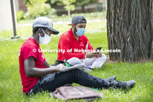Mark Iradukunda works on his laptop and Aldi Airori checks his phone while wearing masks and practic