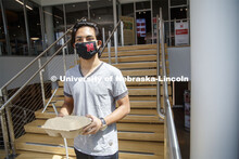 A young man wearing a Husker mask gets takeout dining from the Willa Cather Dining Center. Photo sho