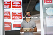 A young man wearing a Husker mask gets takeout dining from the Willa Cather Dining Center. Photo sho