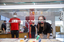 A young woman leans in toward the food bar to select her lunch at the Willa Cather Dining Center. Ph