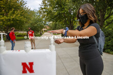 Photo shoot of students on city campus practicing hand sanitizing. A young woman stops at a hand san