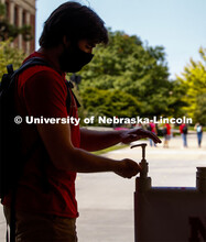 Photo shoot of students on city campus display mask wearing and hand sanitizing. A young man stops a