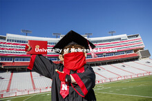 A masked Herbie Husker holding a diploma, poses in regalia to announce spring commencement will be i