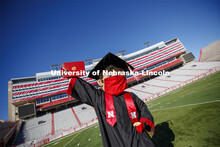 A masked Herbie Husker holding a diploma, poses in regalia to announce spring commencement will be i