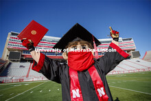 A masked Herbie Husker holding a diploma, poses in regalia to announce spring commencement will be i