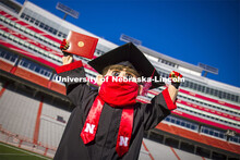 A masked Herbie Husker holding a diploma, poses in regalia to announce spring commencement will be i