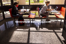 Gabriella Silva (red mask) and Zoe Keese (white mask) study at the tables in the sun lit lobby insid