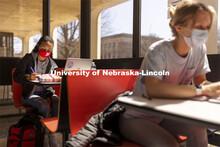 Gabriella Silva (red mask) and Zoe Keese (white mask) study at the tables in the sun lit lobby insid