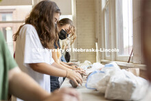 Jena Nelson, a sophomore from Omaha, looks over to a classmate as they wedge lumps of clay in the be