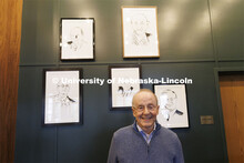 Former Chancellor Harvey Perlman stands in front of framed caricatures of former UNL Chancellors. Ri