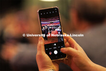 A family member snaps a photo on their phone of their grad marching in for commencement. Graduate co