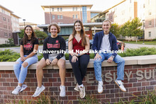 Students seated on a brick wall outside of University Suites Residence Hall. Housing Photo Shoot in 