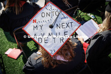 A decorated cap says, "Onto my next adventure". Undergraduate commencement at Memorial Stadium. May 