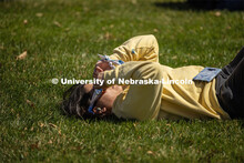A student relaxes on the East Campus Mall grass as they look skyward at the eclipse. April 8, 2024. 