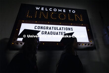 Graduates are silhouetted in front of a marquee in the hallways in Pinnacle Bank Arena. Graduate Com